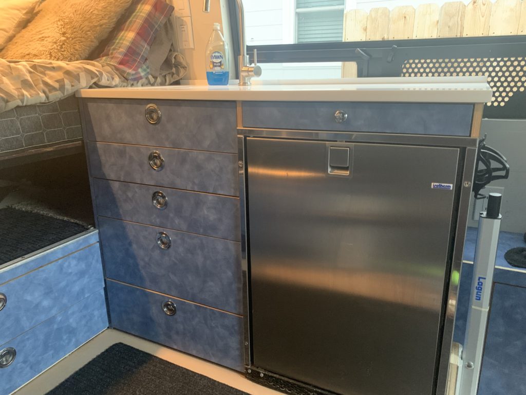 The full kitchen features an induction cooktop, fridge, and built-in sink with hot water.